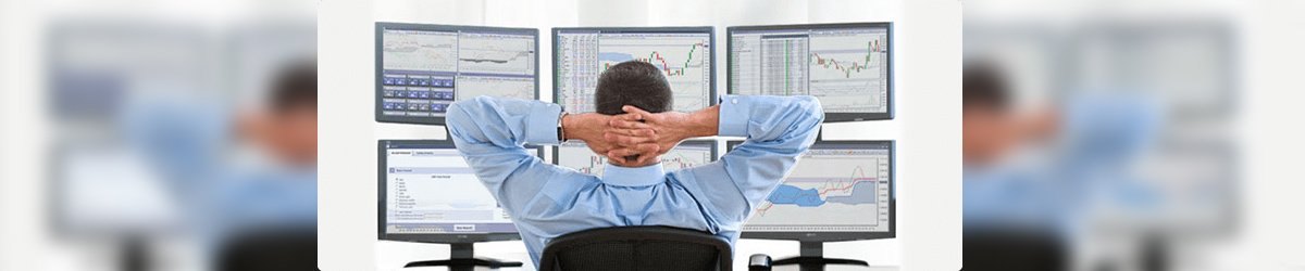 На картинке изображены мониторы, на экранах которых биржевые графики, и человек, который сидит перед ними и анализирует рынок.